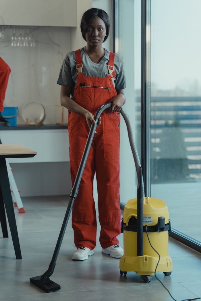 Une femme adulte en combinaison rouge manie un aspirateur dans un intérieur moderne, en se concentrant sur les tâches de nettoyage.